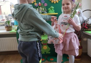 Widok na chłopca wręczającego dziewczynce tulipana i torebkę z prezentem.